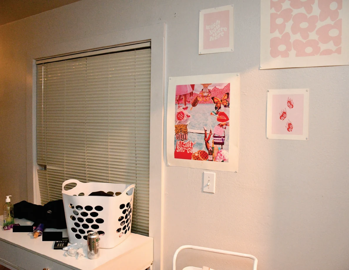 Laundry basket on a white desk beneath window blinds and pink wall artwork.