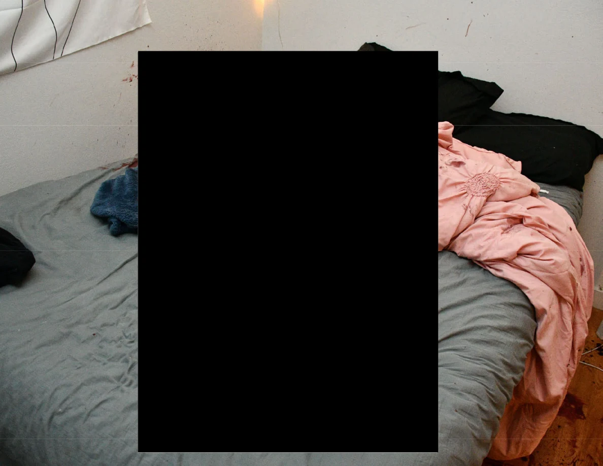 Bed with gray sheet, pink fabric and blue blanket mostly obscured by a large redaction.