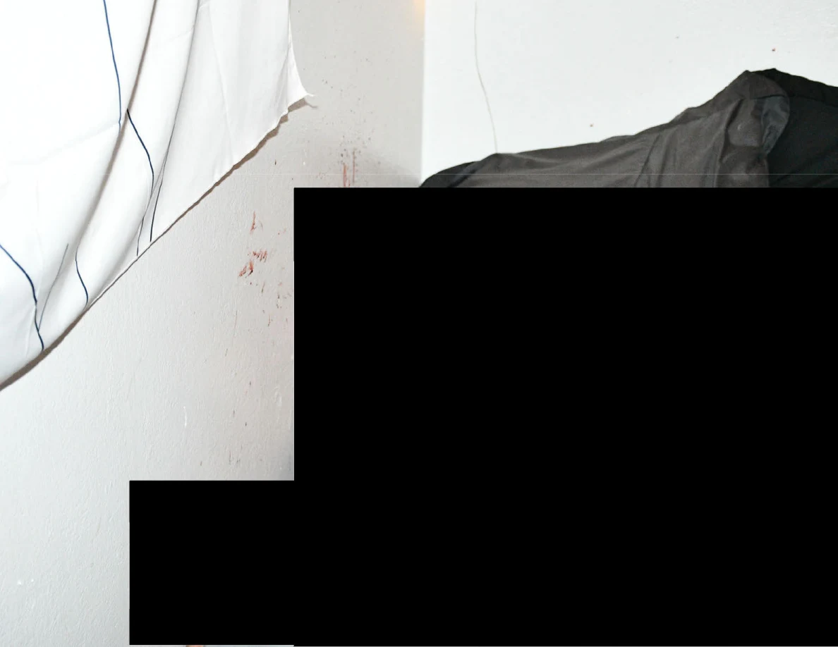 Reddish marks on a pale wall beside dark bedding, with most of the image redacted.