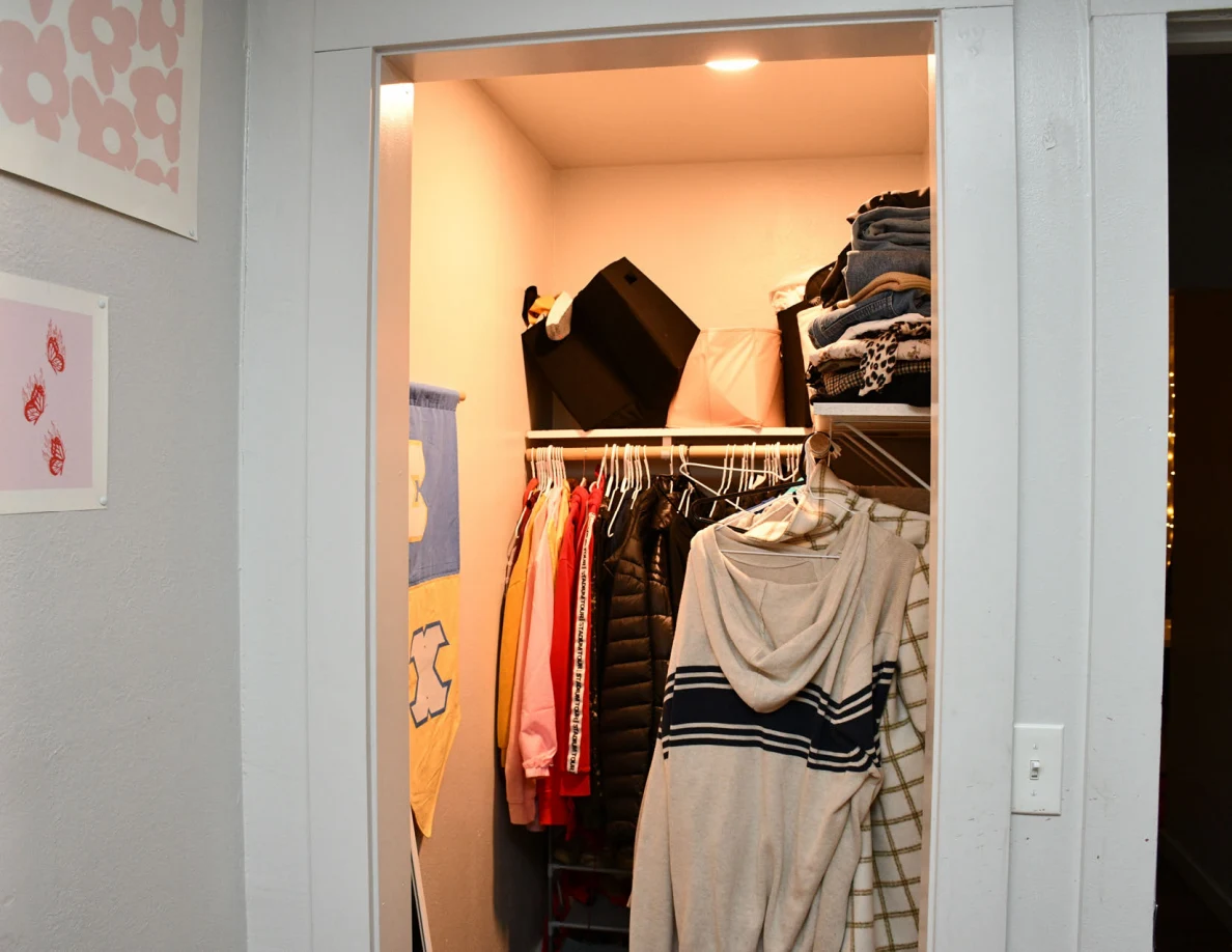 Lit closet with clothing on hangers and folded garments on upper shelves.