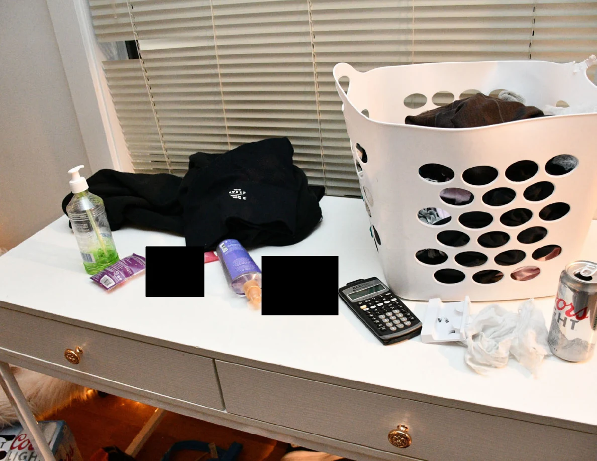 White desk with laundry basket, calculator, bottles and clothing, with small redactions.