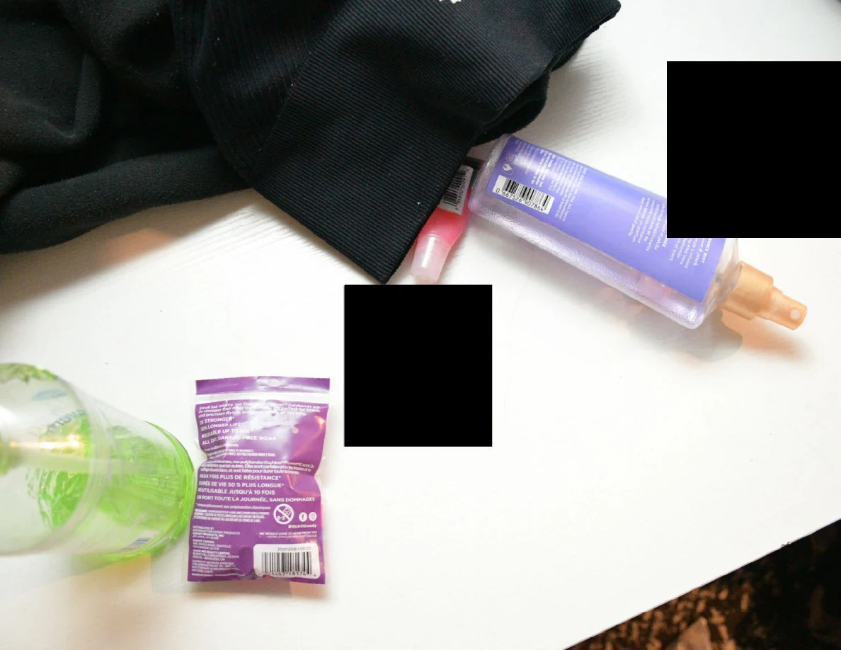 Close view of toiletry bottles, a purple packet and dark fabric on a desk with redacted items.