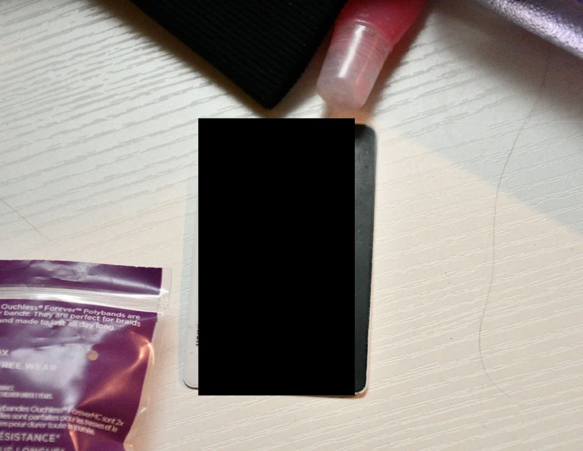 Partly redacted phone-shaped object on a white desk beside a small spray bottle and packet.