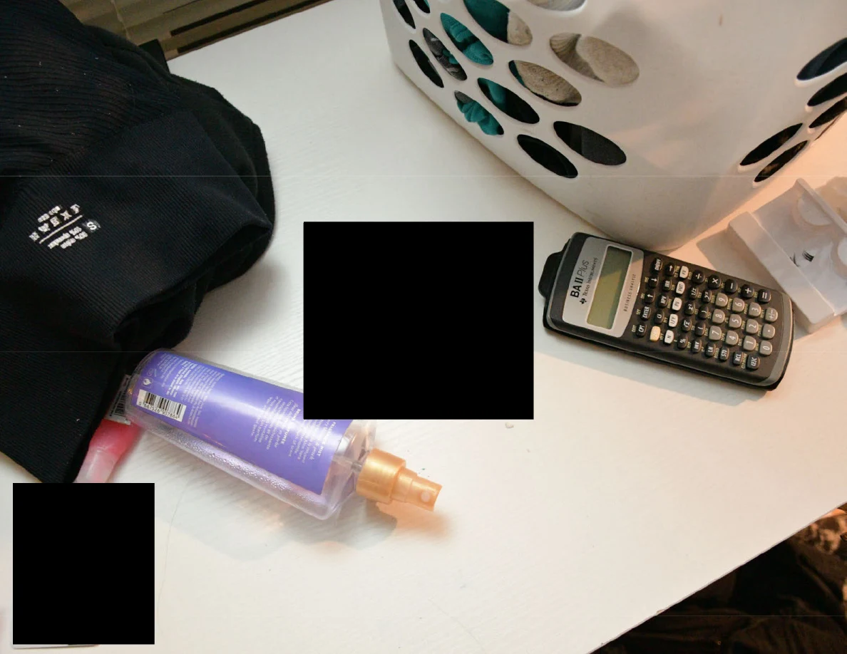 Calculator beside laundry basket and toiletries on a desk with black redactions.