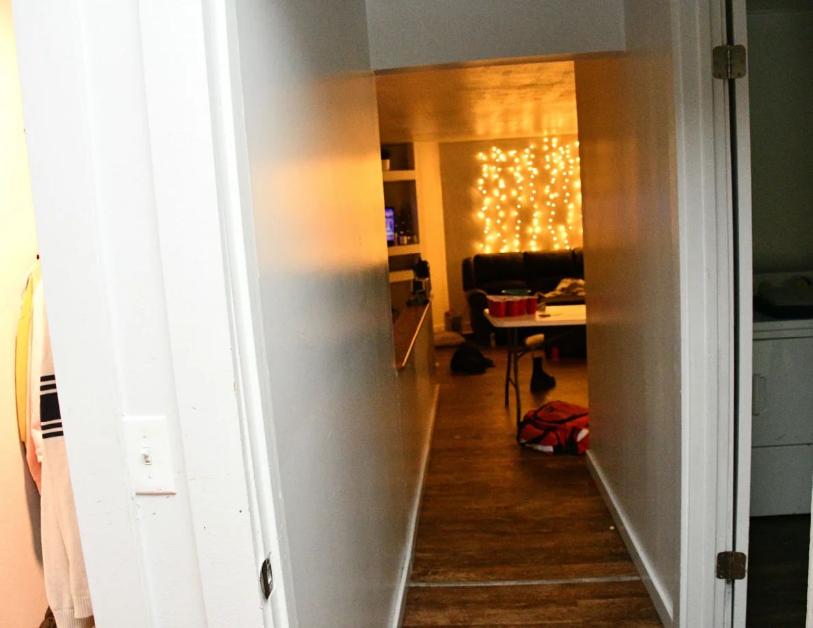 Hallway looking toward a living room with string lights, sofa and a table with red cups.
