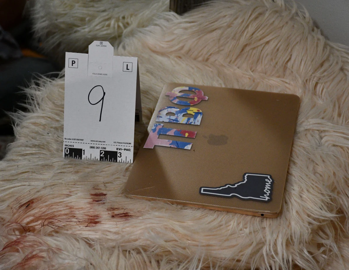 Closed gold-colored laptop with stickers on a fluffy pale chair beside scale card 9 and reddish marks.
