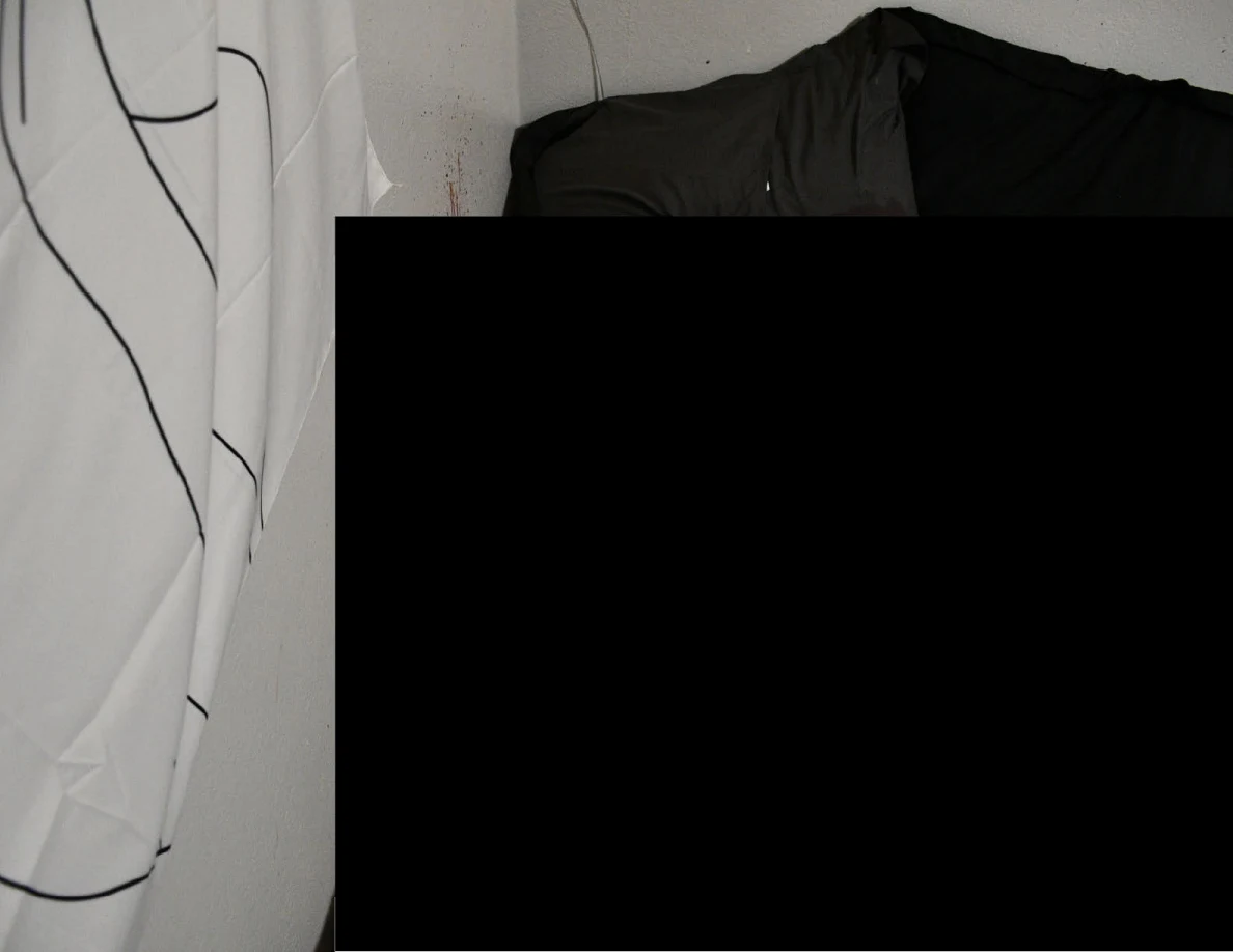 Pale wall and dark bedding beside a figure wall hanging, largely obscured by a black redaction.