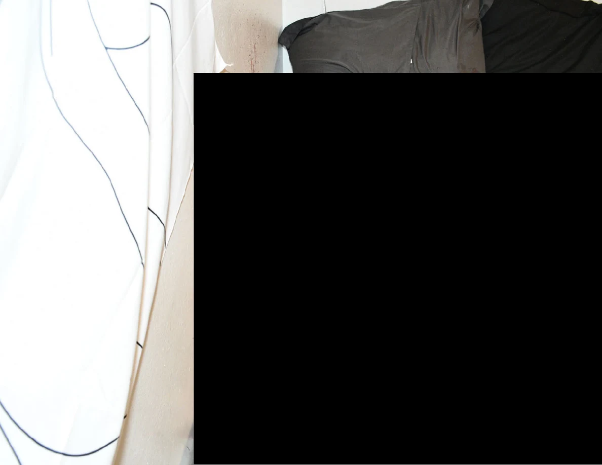 Brighter close view of wall and dark bedding beside a wall hanging, with large redaction.
