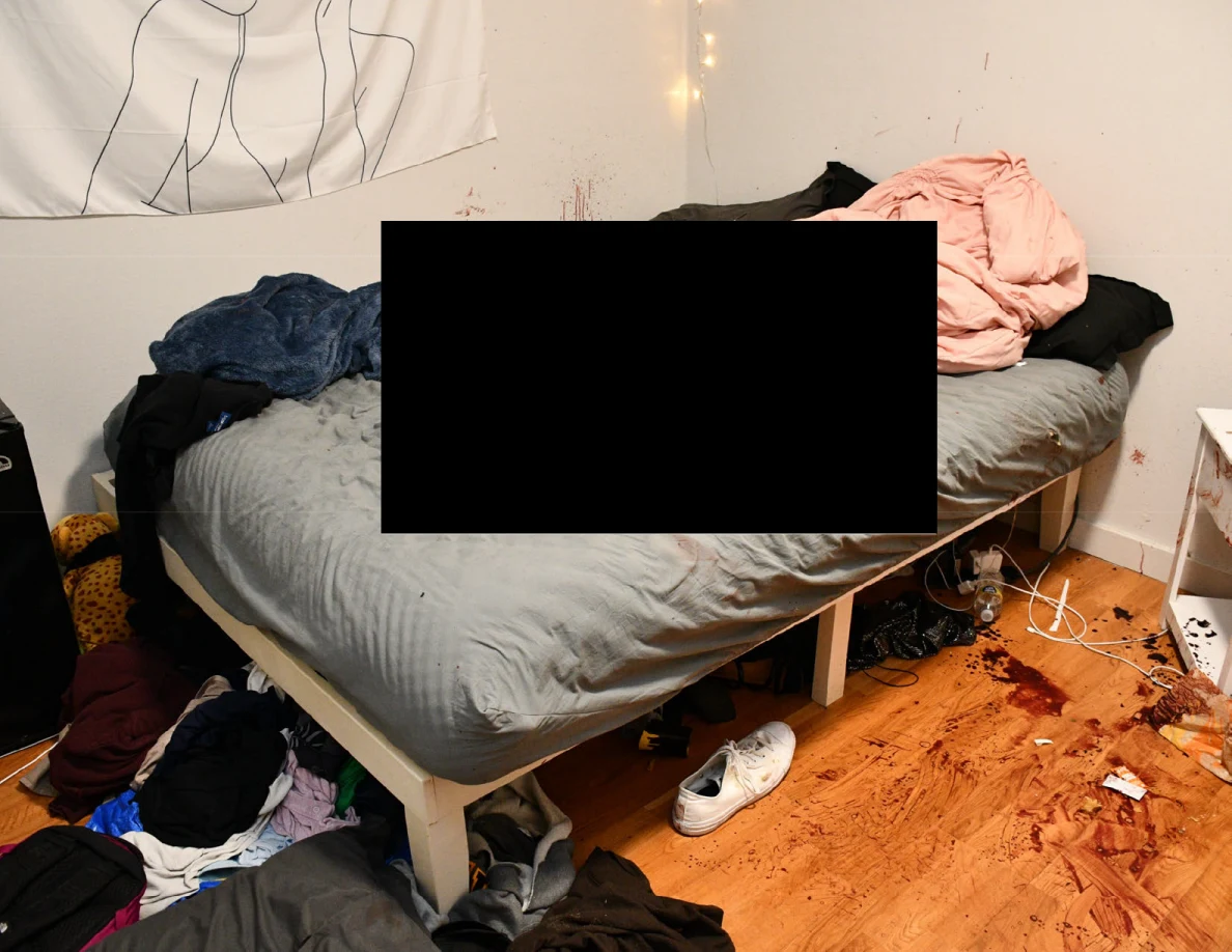 Gray-covered bed with blankets and a large redaction above scattered shoes and marked flooring.