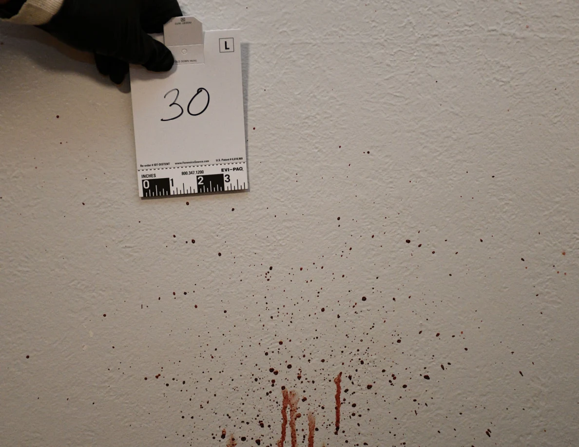 Scale card 30 held beside reddish spots and streaks on a textured wall.