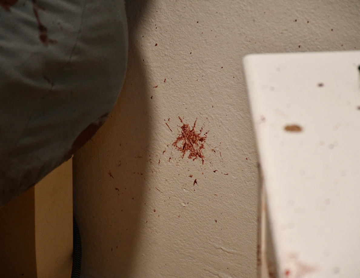 Close view of a small reddish star-shaped wall mark between bedding and a white cabinet.