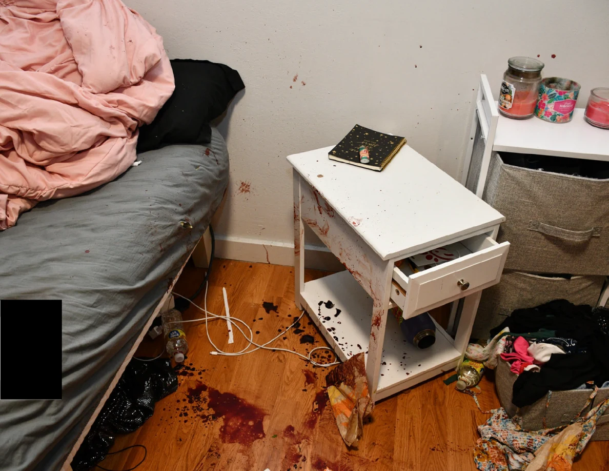 White bedside cabinet with partly open drawer beside marked flooring and the edge of a bed.