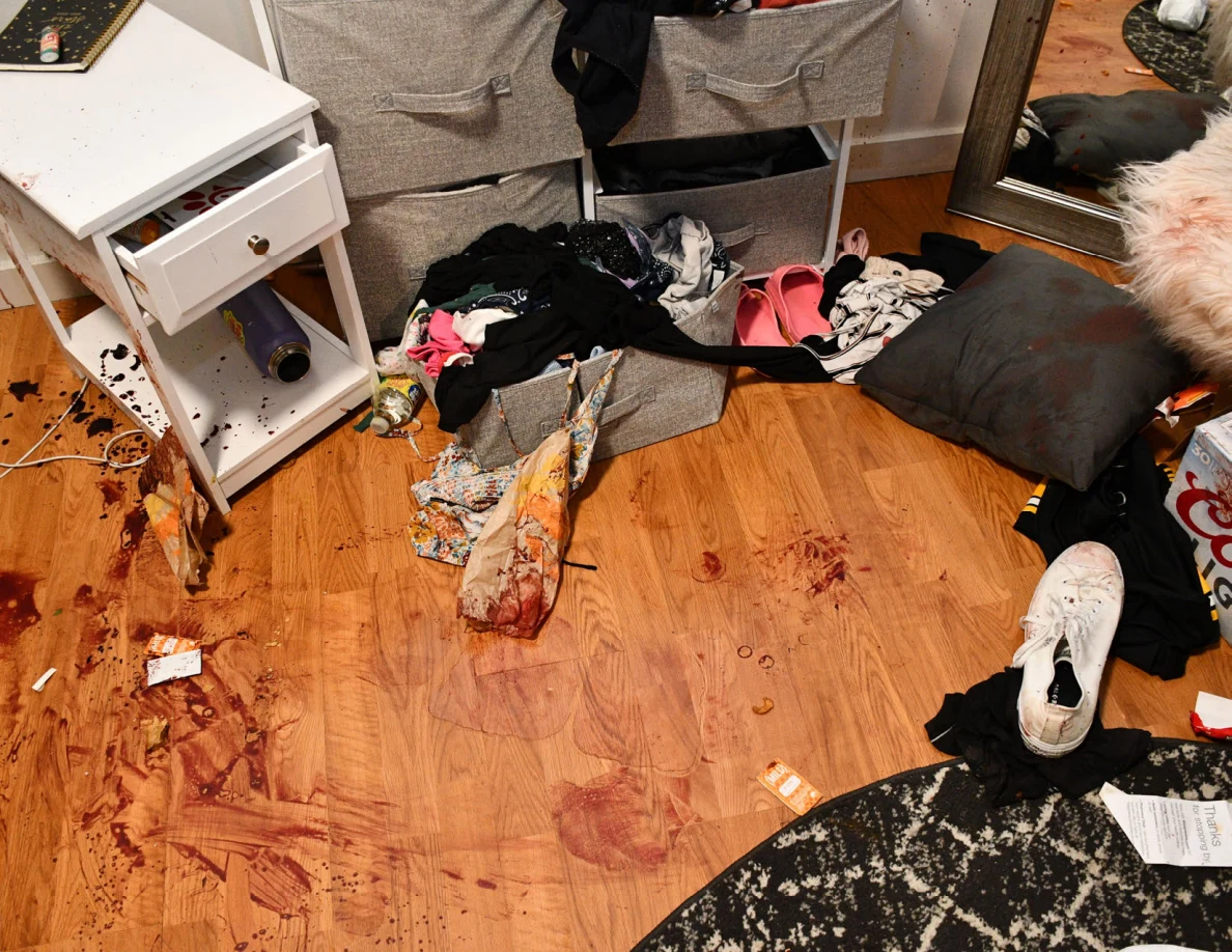 Bedroom floor with reddish marks among fabric drawers, clothing, shoes and a dark pillow.