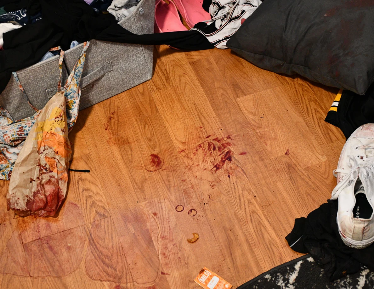 Close view of reddish floor marks, a patterned bag and scattered footwear and clothing.