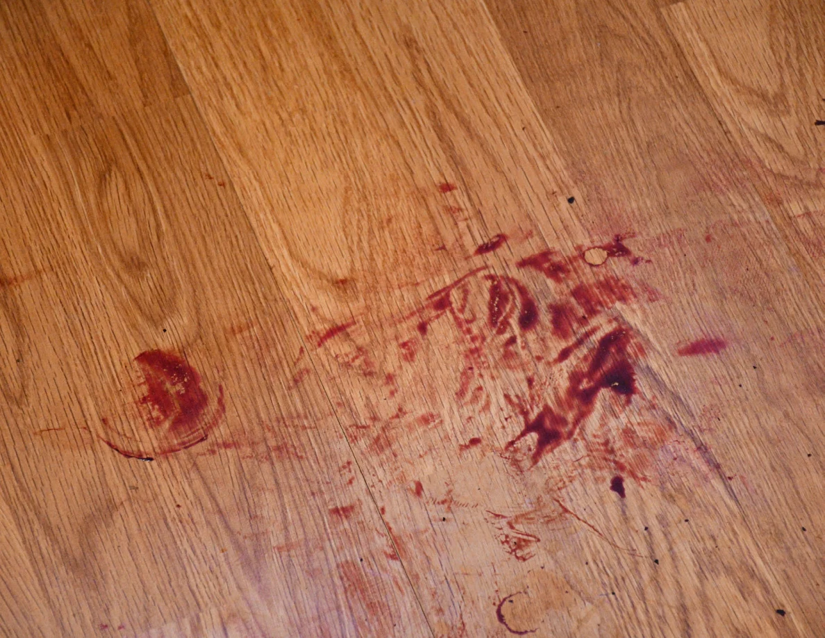 Close view of reddish smeared and ring-shaped marks on wood-pattern flooring.