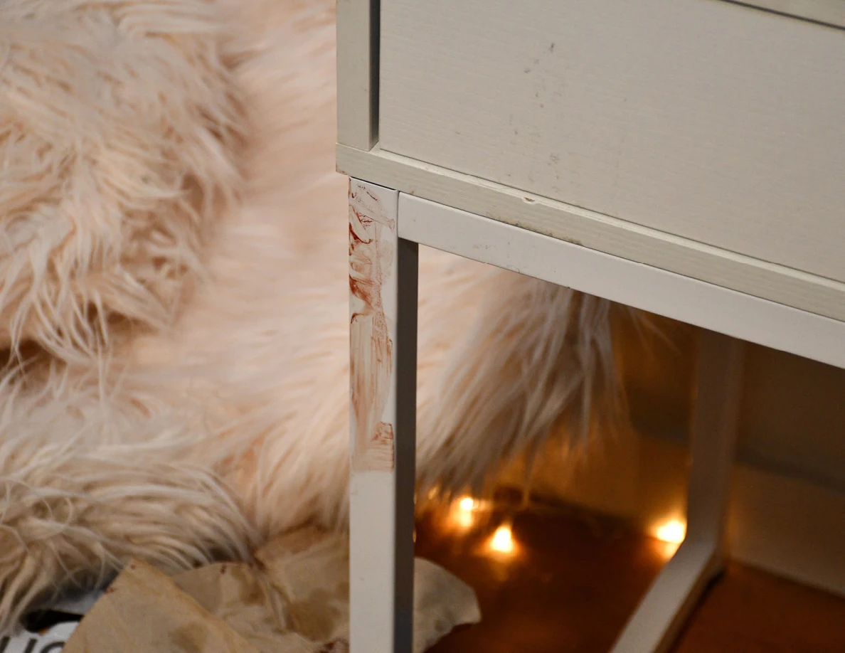 Reddish smears on a white desk leg beside a fluffy chair.