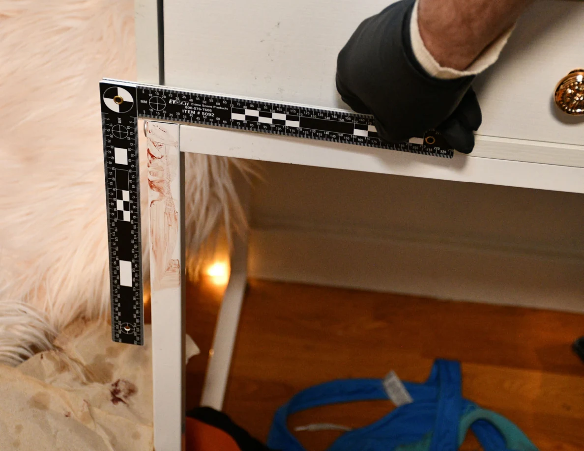 L-shaped measuring scale around reddish marks on a white desk leg.
