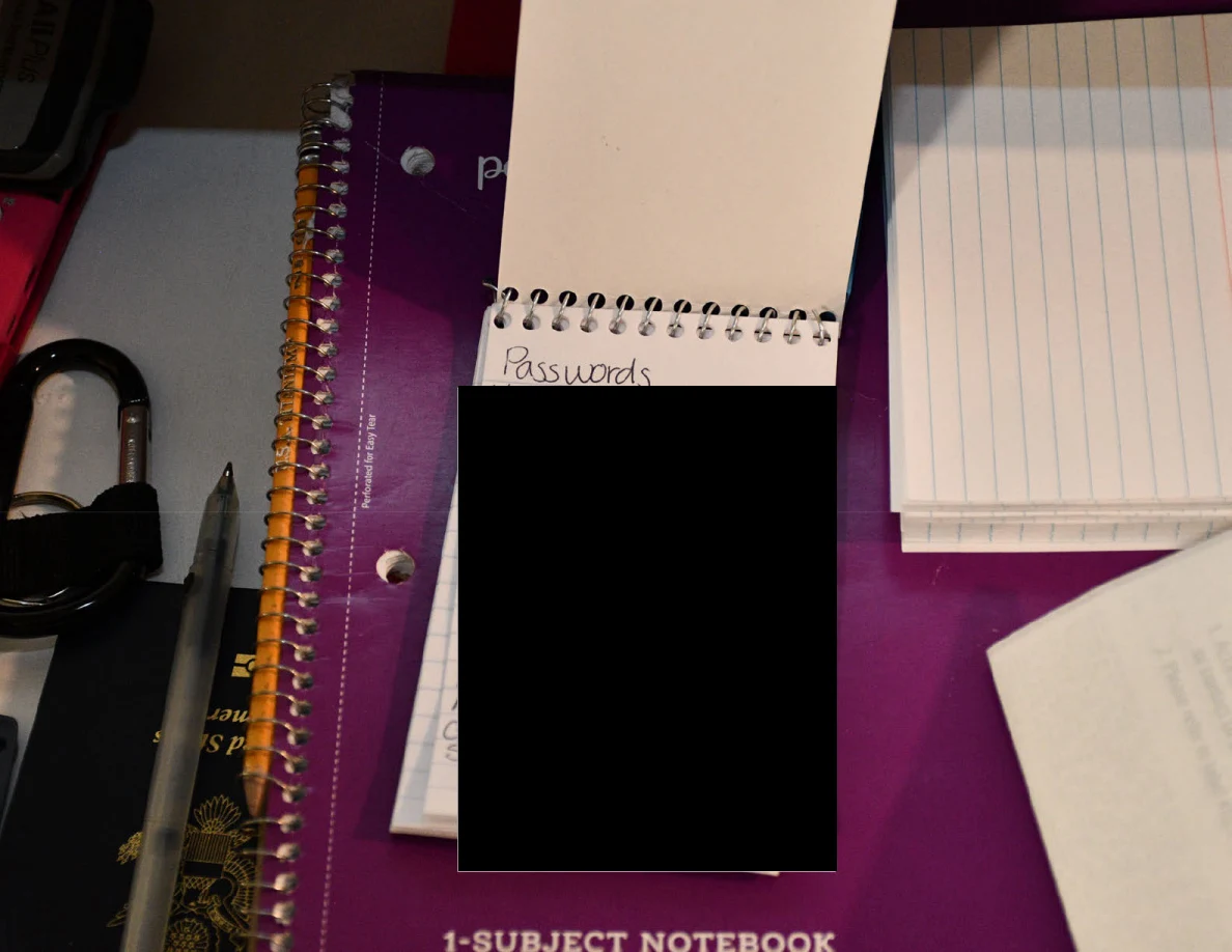 Small spiral pad headed Passwords with its contents blacked out on a purple notebook.