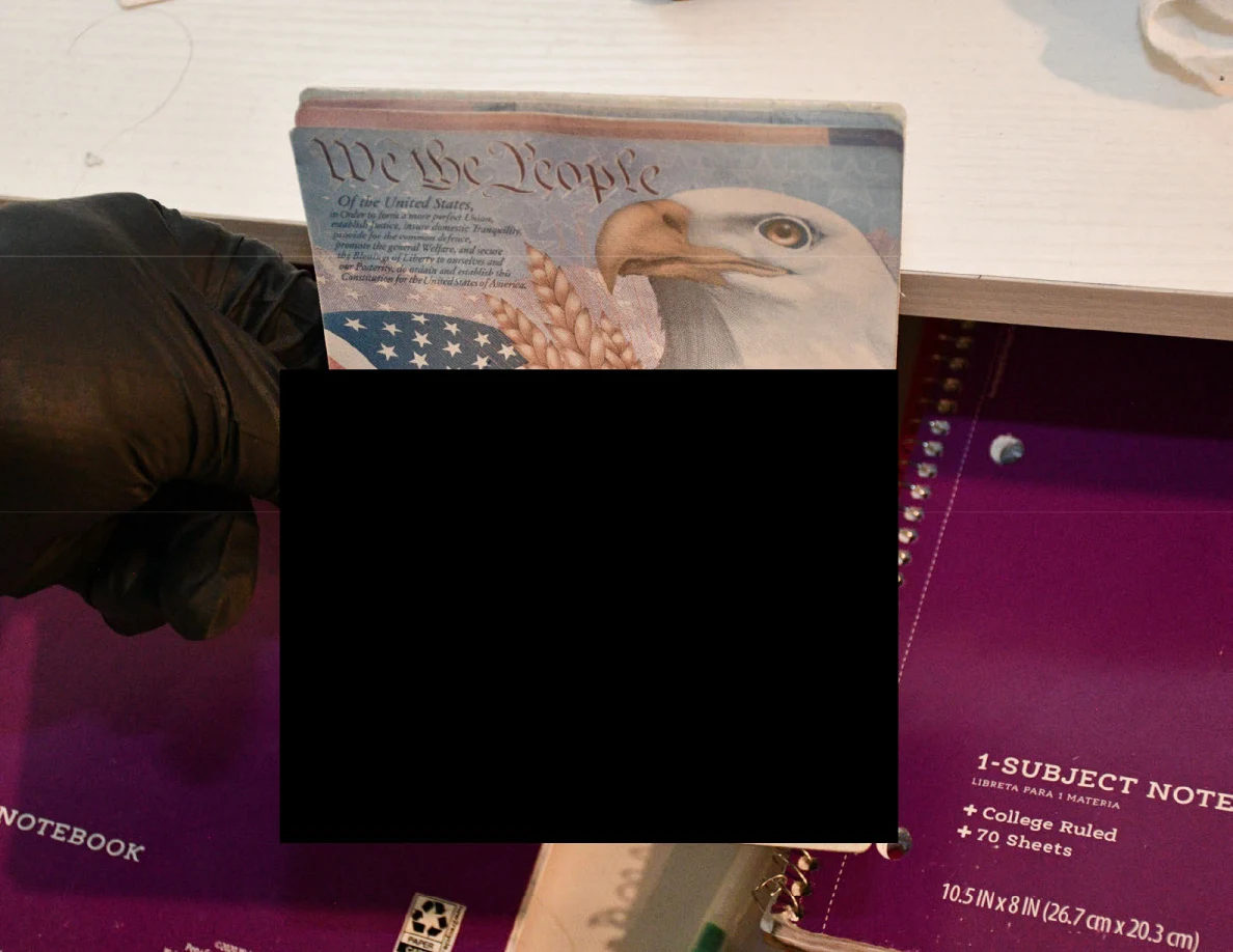 Black-gloved hand holding an eagle-and-flag card with most text redacted.