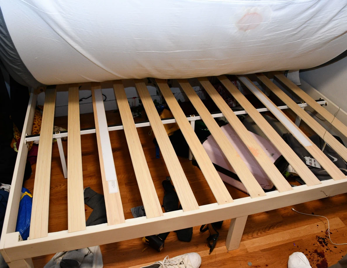 Raised mattress revealing wooden bed slats and pale marks on the mattress.