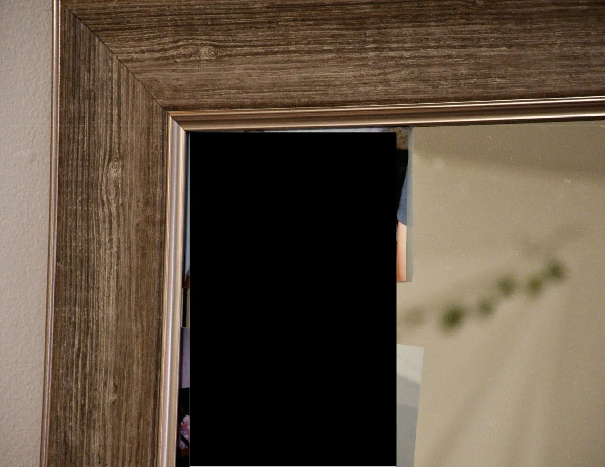 Upper corner of a wood-look mirror frame beside a black redaction.