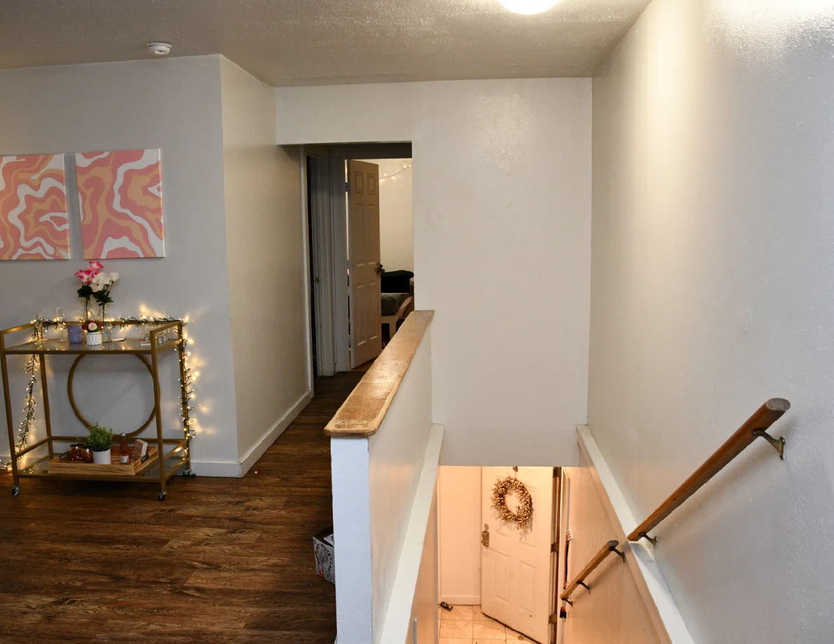 Upstairs landing with a gold drinks cart, pink wall art and stair railing.