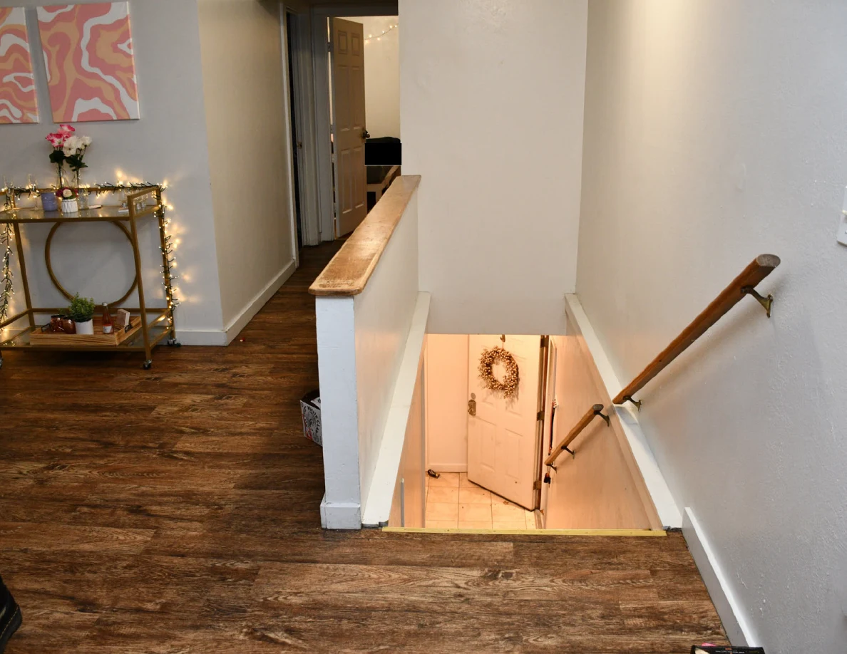 Stairwell descending toward a door with a wreath beside a gold drinks cart.