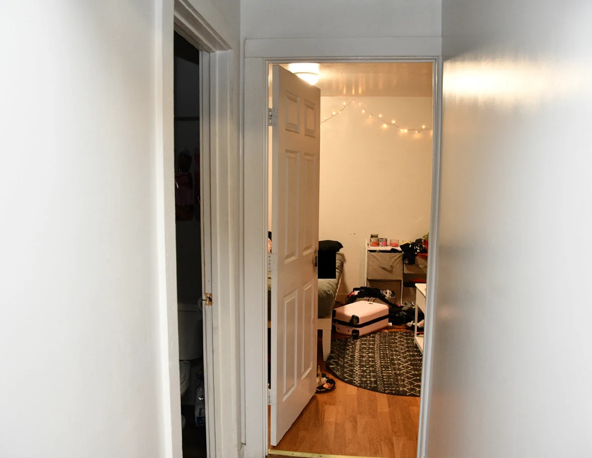 Hallway through an open bedroom door with string lights and a pink suitcase.
