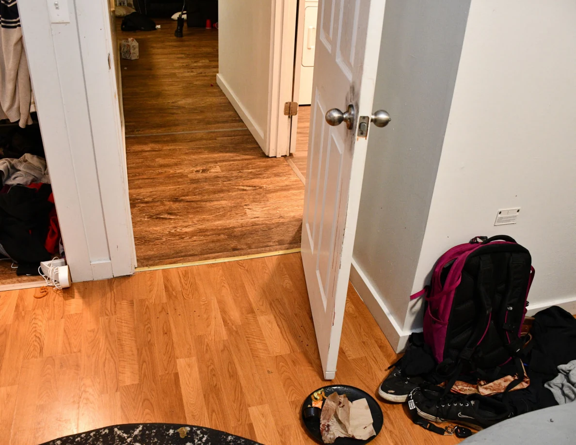 Open bedroom doorway with a dark pink-trimmed backpack and clothing on the floor.