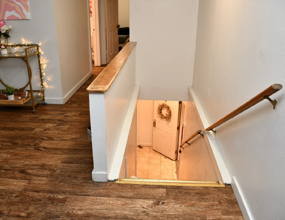 Upstairs stair opening with wooden handrails and a lower door decorated with a wreath.