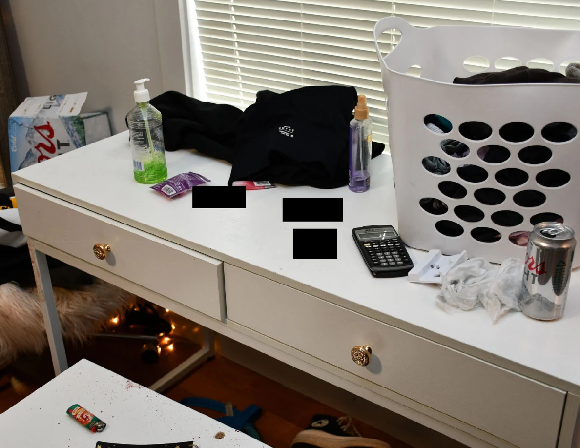 White desk with laundry basket, calculator, drink can and bottles, with several small black redactions.
