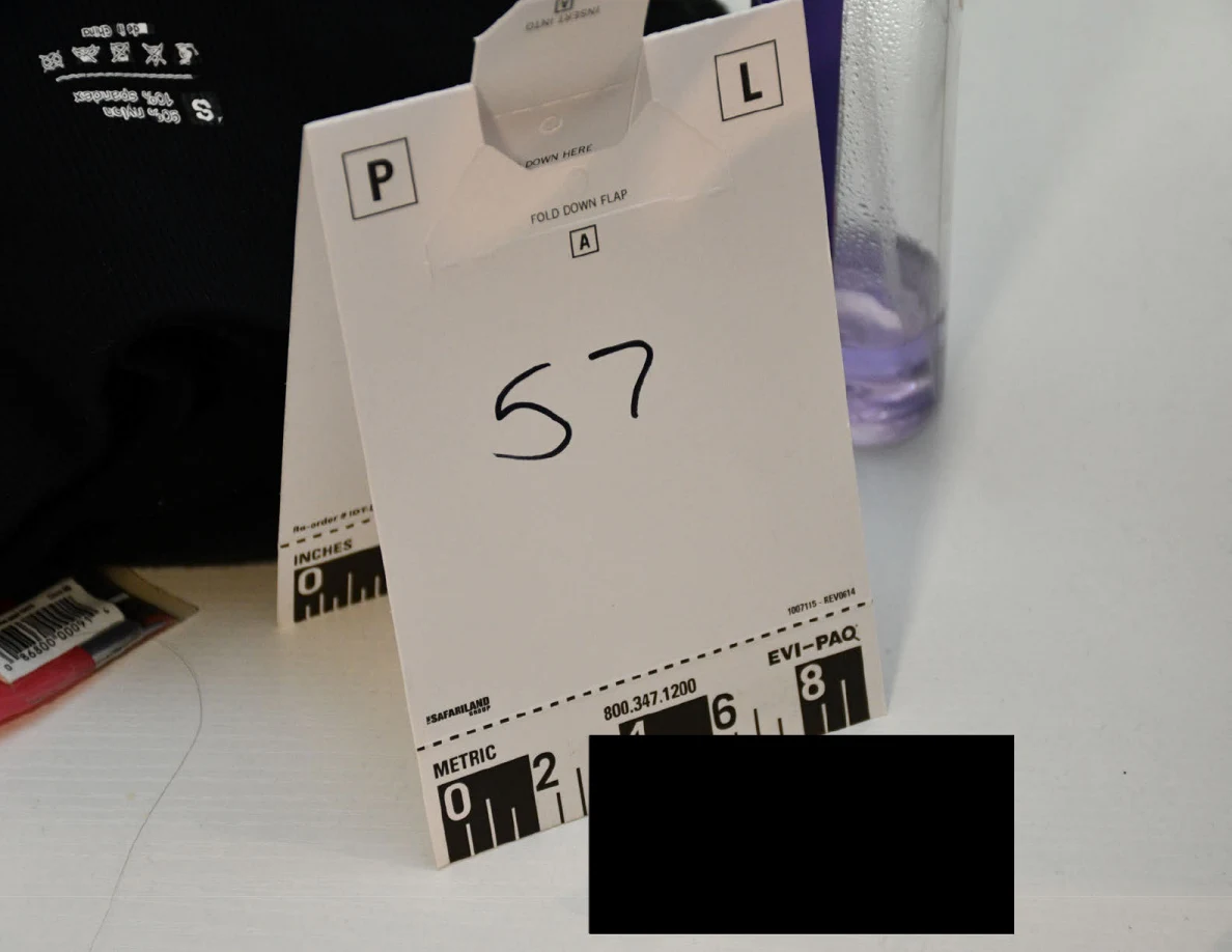 Scale card 57 on a white desk beside dark fabric and a purple bottle, partly redacted.