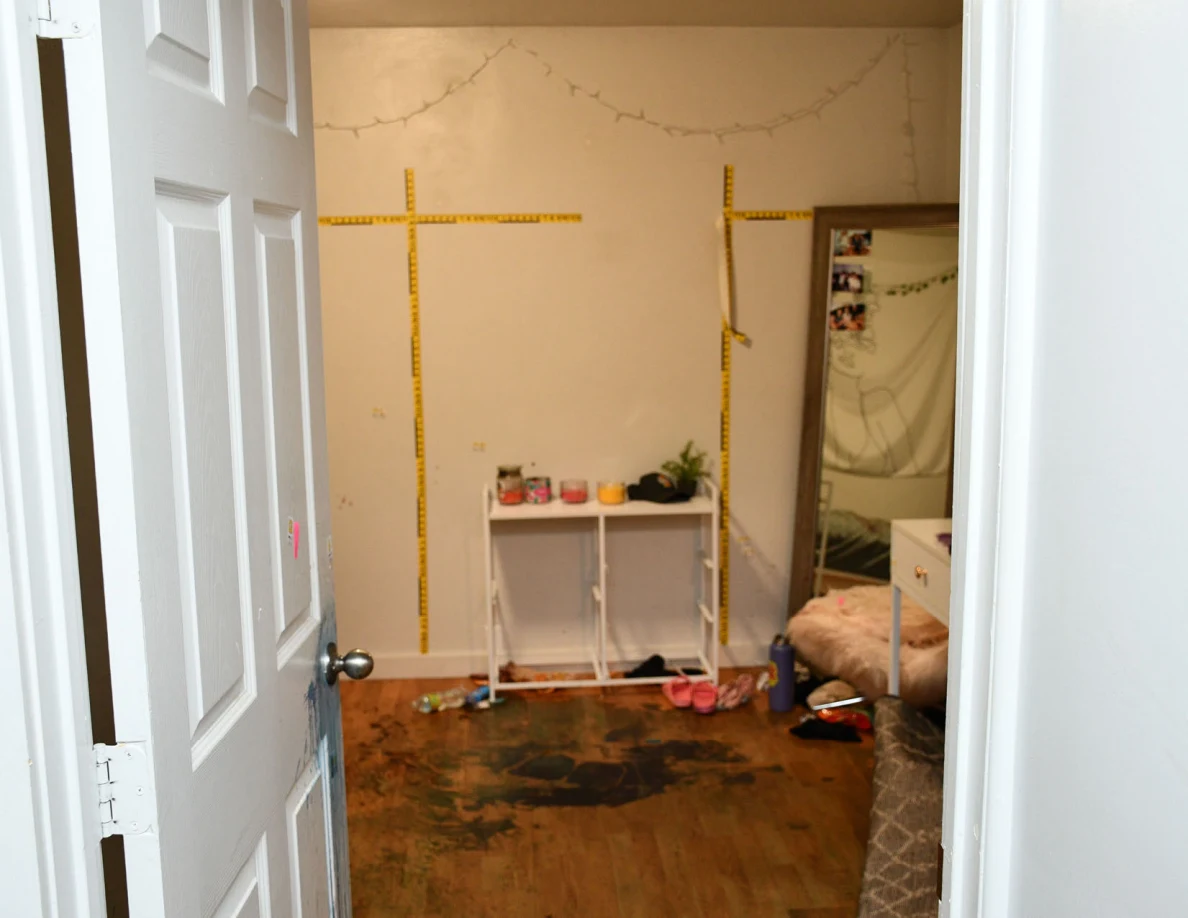Bedroom doorway looking toward yellow wall measuring scales, a mirror and reddish floor marks.