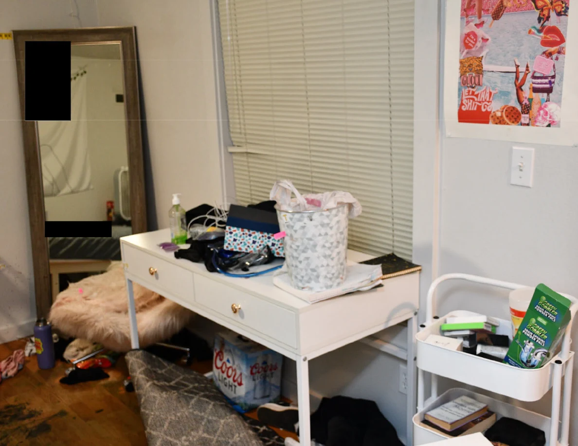White desk beneath closed blinds with bags and a patterned basket beside a rolling cart.