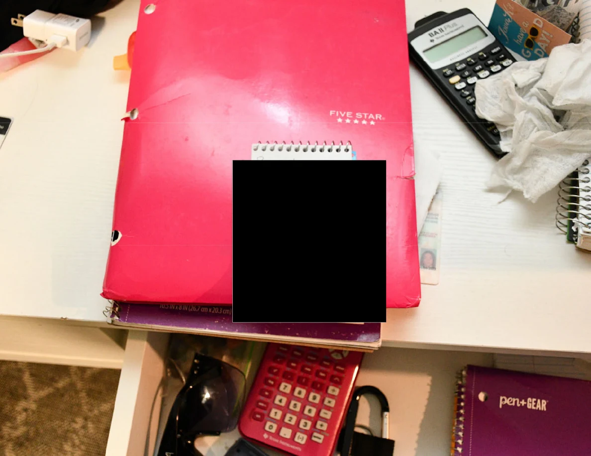 Pink notebook and calculators beside an open drawer, with a small spiral pad blacked out.