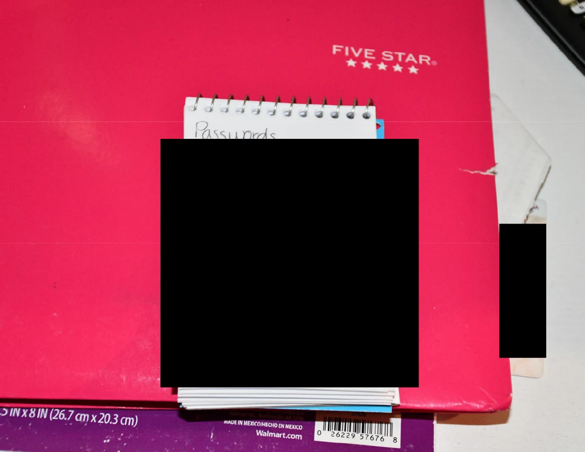 Close view of a spiral pad headed Passwords with its contents blacked out on a pink notebook.
