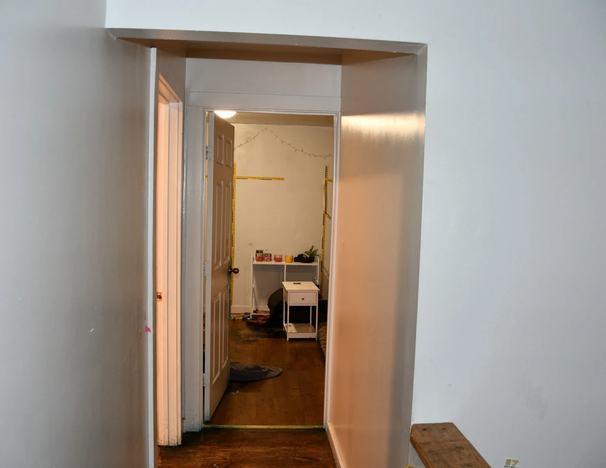Hallway looking through a bedroom doorway toward yellow wall scales and white furniture.