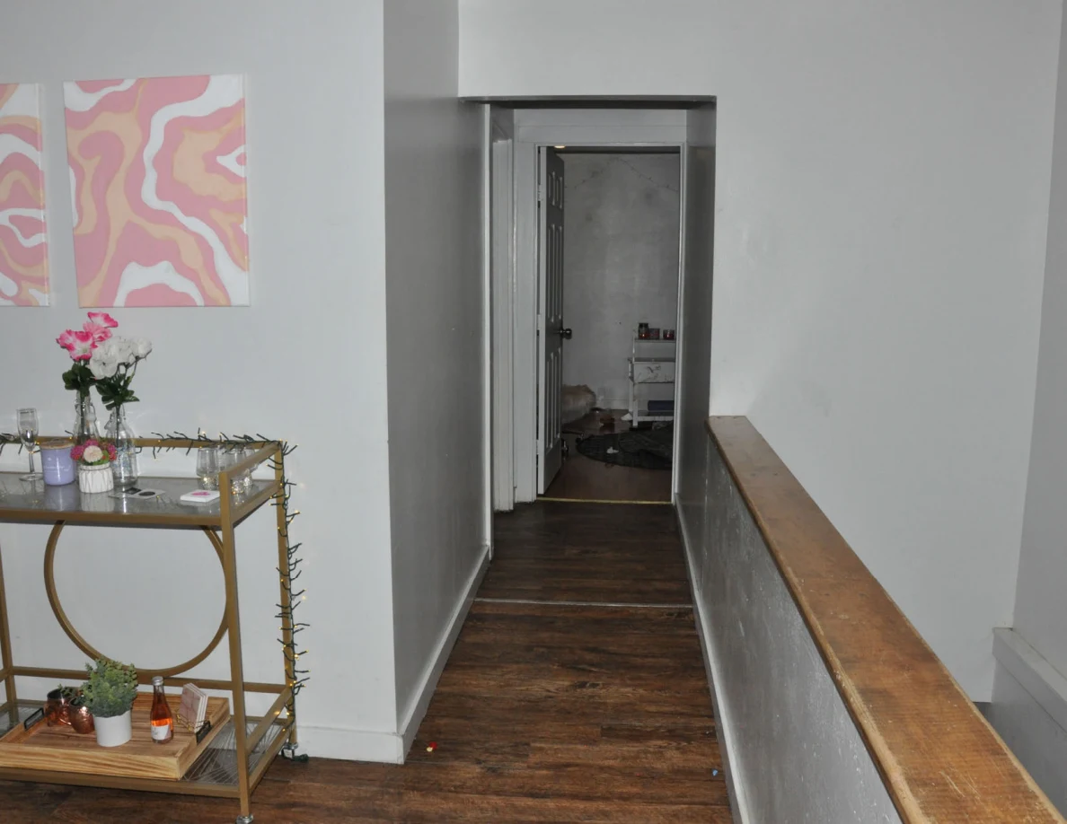 Hallway beside a gold drinks cart, pink wall art and wooden stair rail.