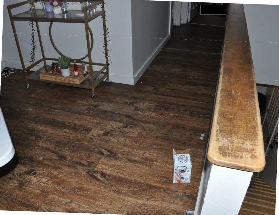 Wood-pattern landing floor beside a drinks cart, wooden stair rail and upright carton.