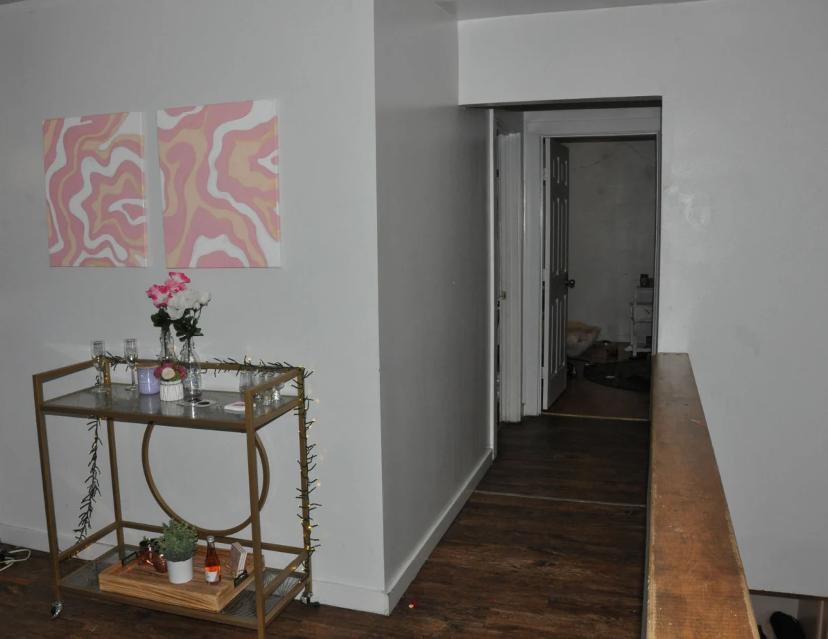 Gold drinks cart below pink wall art beside a hallway.