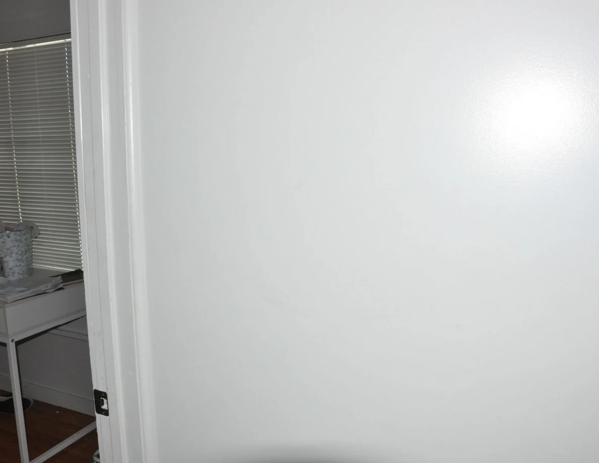 White wall beside a bedroom door frame with closed blinds visible inside.