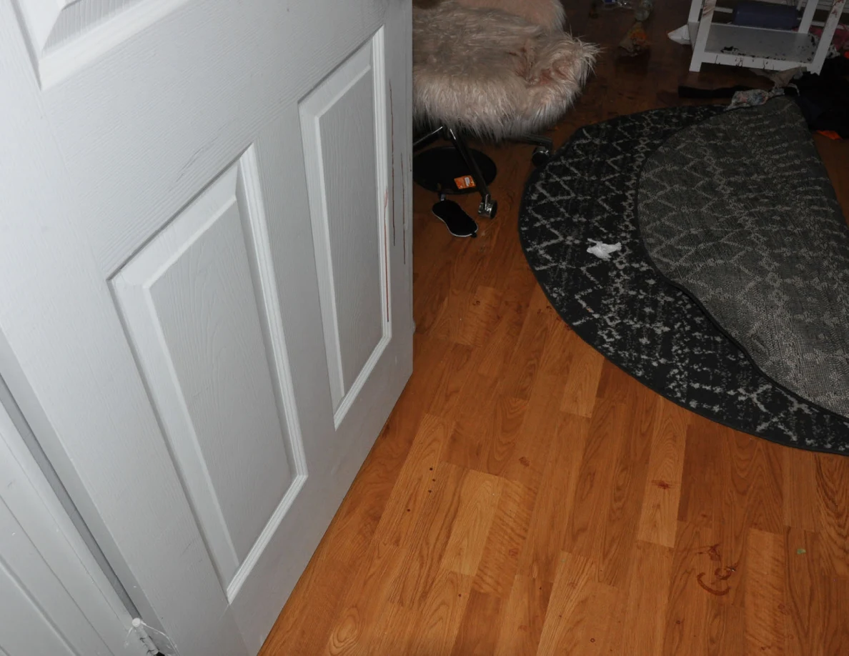 Open white bedroom door above wood-pattern flooring and a folded patterned rug.