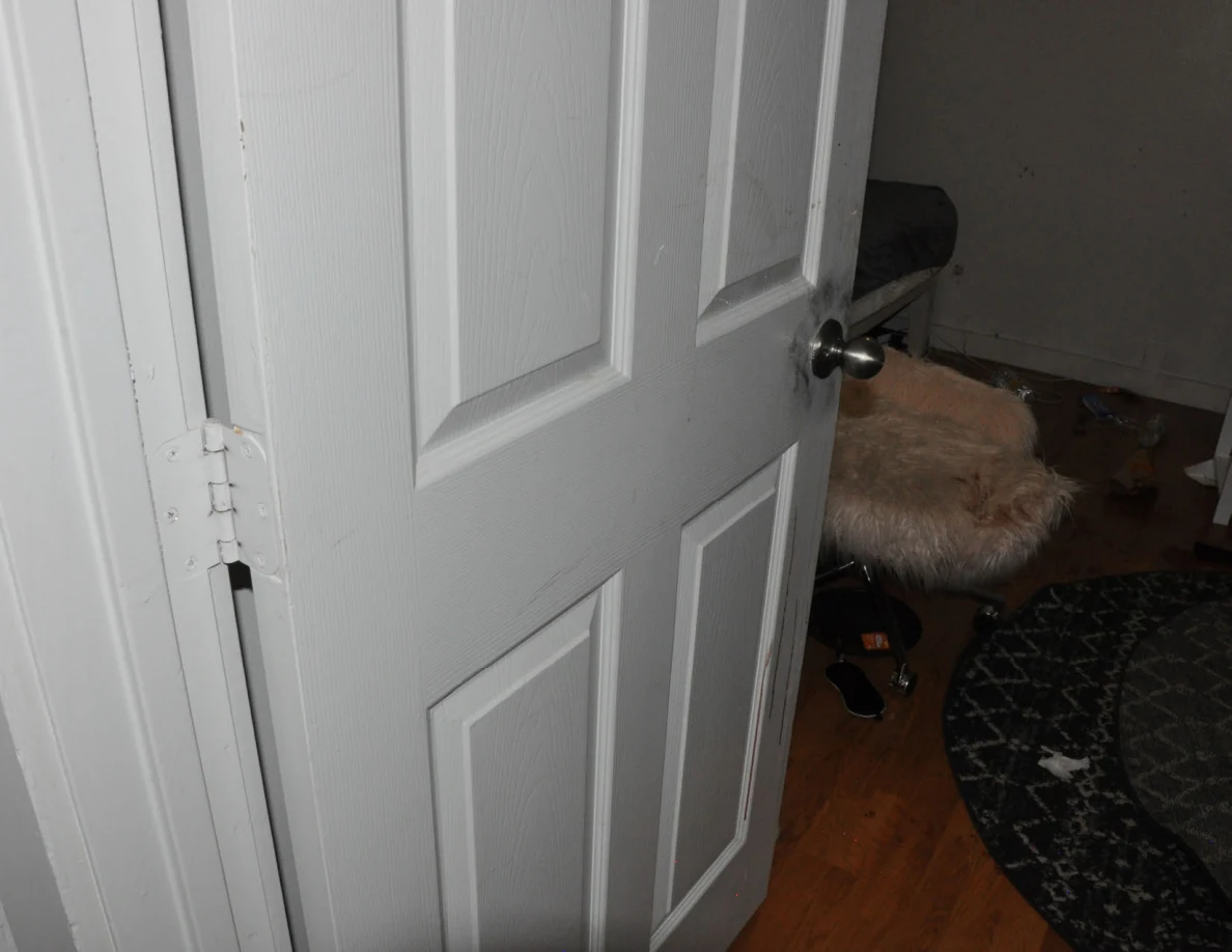 Open white paneled bedroom door beside a fluffy chair and folded patterned rug.