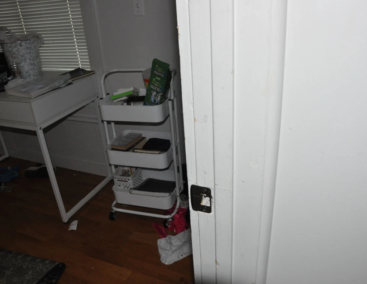 Door latch plate beside a white rolling cart and desk inside a bedroom.