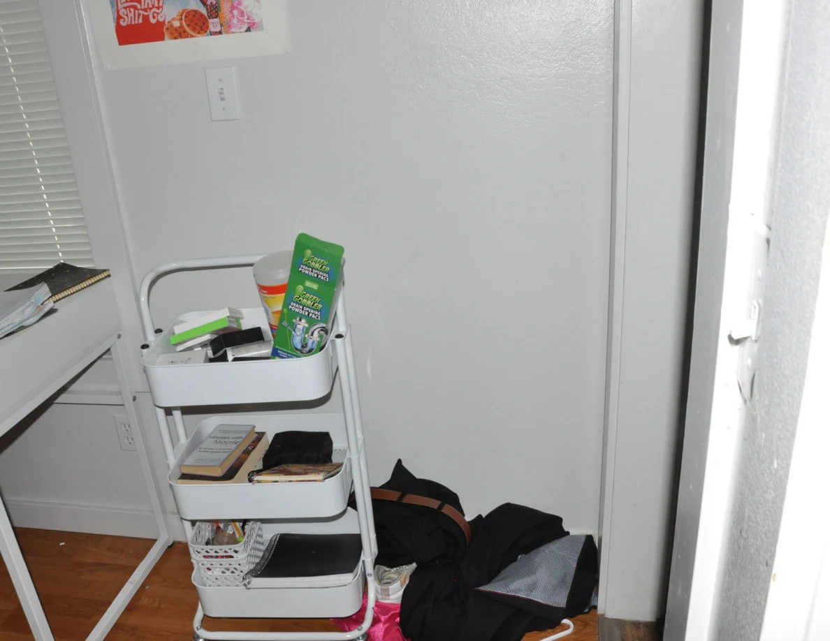 White rolling cart holding books and cleaning products beside dark clothing.