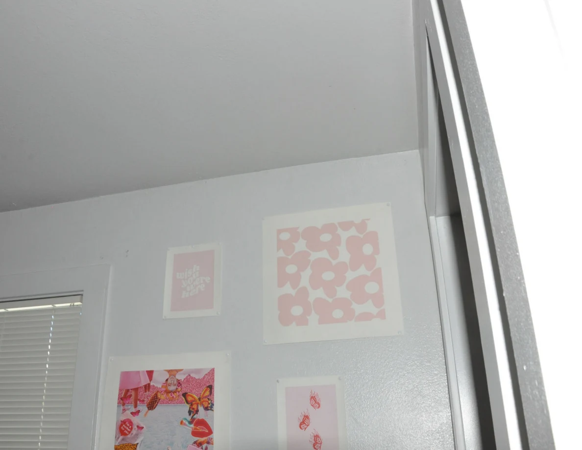 Upper bedroom wall with pink decorative prints beneath the ceiling.