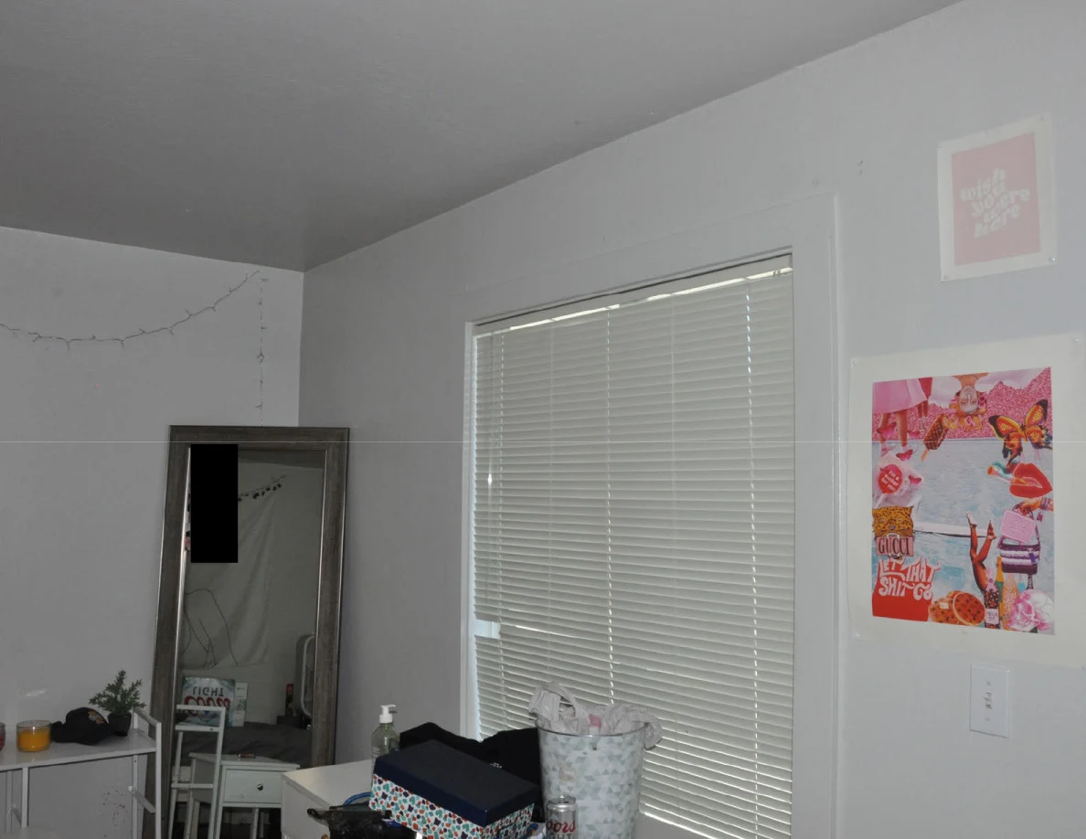 Closed blinds and pink wall art beside a tall mirror and white desk.