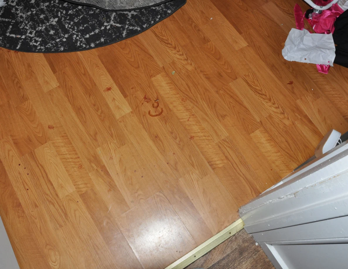 Wood-pattern bedroom flooring with reddish marks beside a doorway threshold.