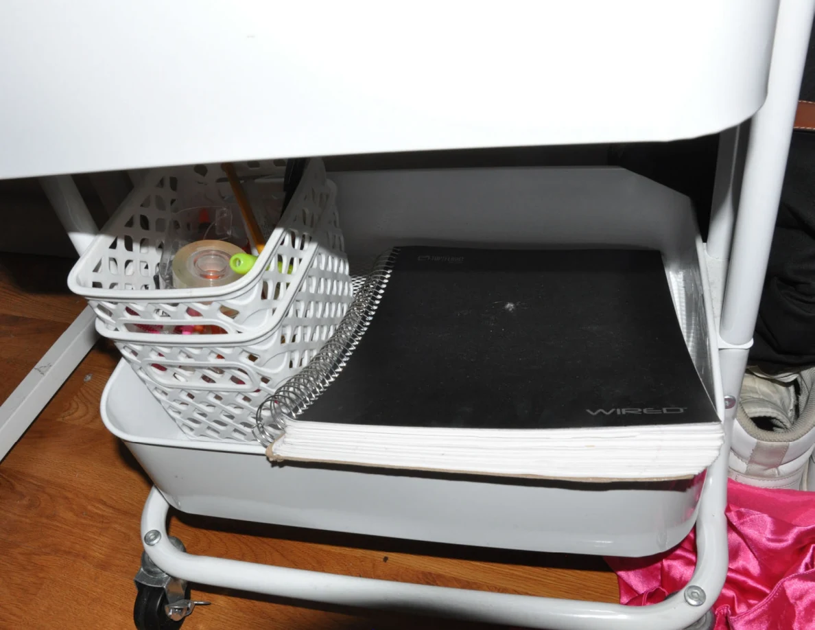 Lower cart shelf with a black spiral notebook and small white basket.