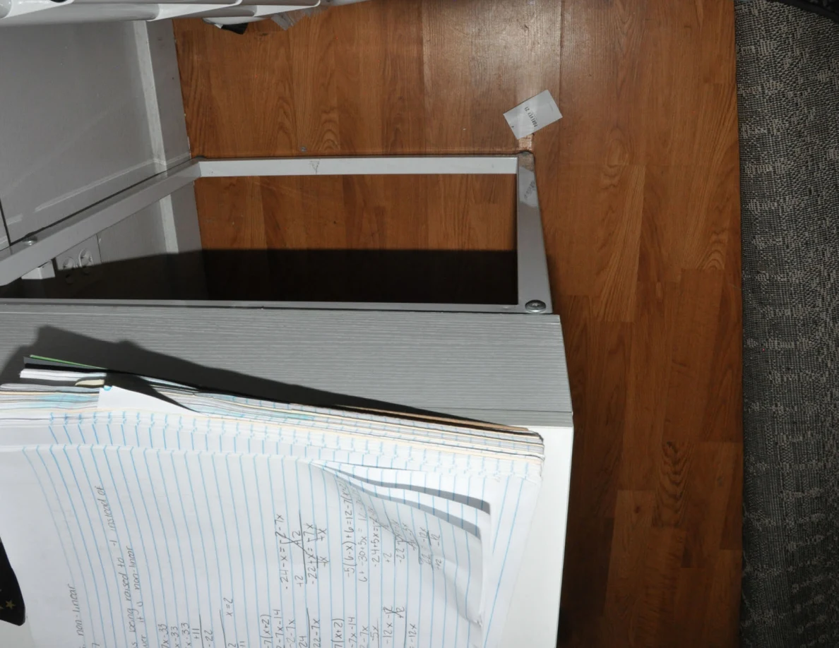 Open lined notebook at the edge of a white desk above wood-pattern flooring.